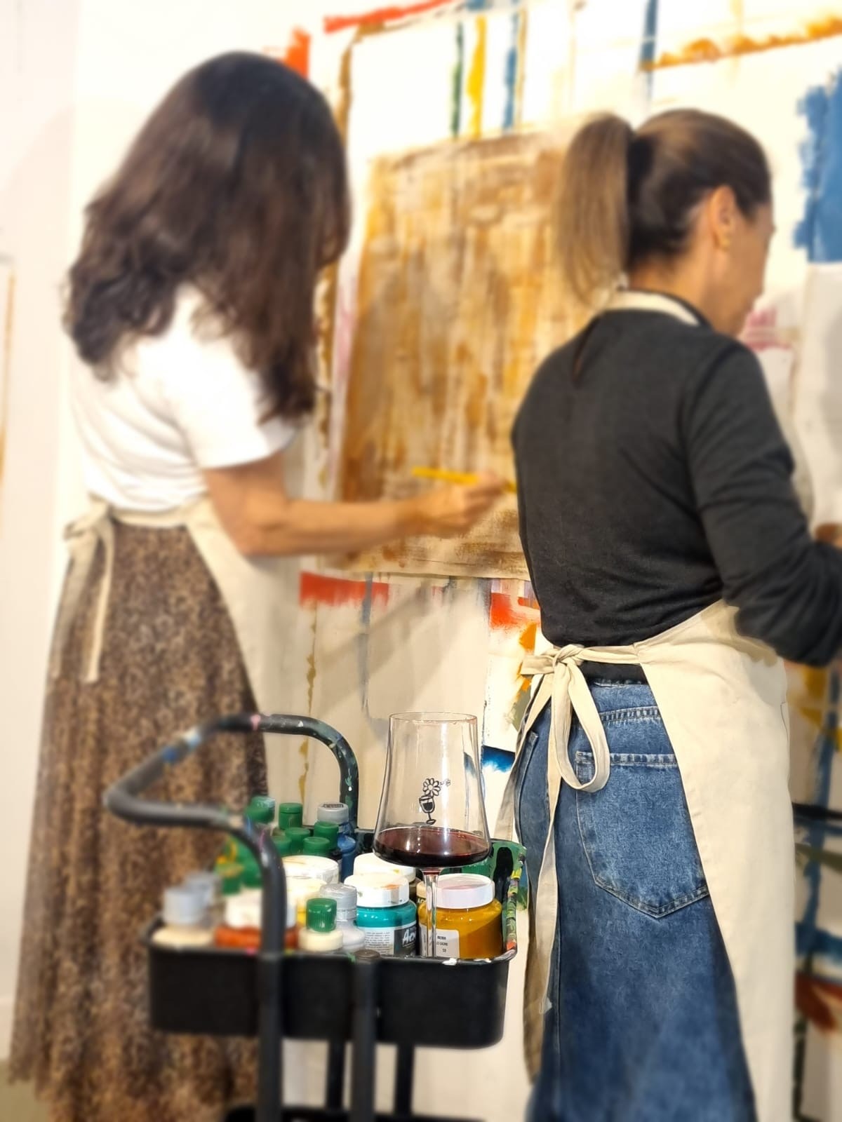 Participantes pintando durante a Vivência Lúdica, com materiais e uma taça de vinho em primeiro plano